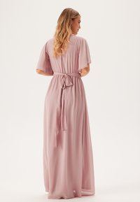 Maxi-jurk in zachtroze stof met korte gefocuste mouwen, een cinched taille en een strikdetail op de rug. Glad textuur en vloeiende ontwerp.