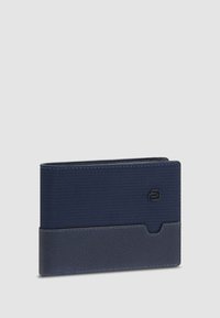 Cartera de marina hecha de tejido texturizado y cuero liso, presenta una forma rectangular delgada y un logotipo sutil en la parte frontal.