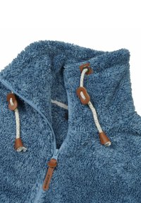 Harige blauwe zip-jack met hoge kraag, voorzien van witte trekkoorden en leren accenten. Zachte textuur en casual ontwerp.