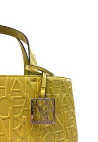 Borsa a tracolla gialla realizzata in materiale testurizzato, con loghi in rilievo, dettagli neri e una targhetta quadrata argentata. Le maniglie sono strutturate e alte.