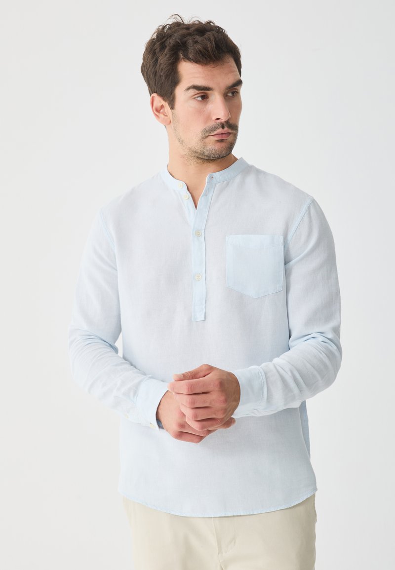 Light blue long-sleeve shirt made of soft fabric, featuring a buttoned Henley neck, a chest pocket, and a curved hemline.