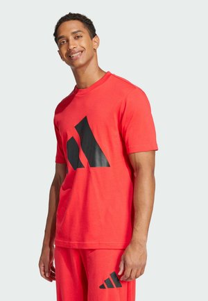 Camiseta de algodón roja con gráfico de logo negro, escote redondo, mangas cortas y corte relajado. Llevada con pantalones rojos a juego.