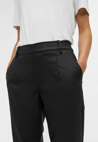 Pantalons noirs ajustés avec une texture lisse, dotés d'une taille, de poches latérales et d'un design à jambe droite. Associés à un haut blanc uni.