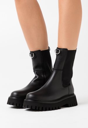 Bottes chelsea en cuir noir avec panneaux latéraux élastiques, garnitures argentées et semelle en caoutchouc épaisse avec un motif de bande de roulement profond.