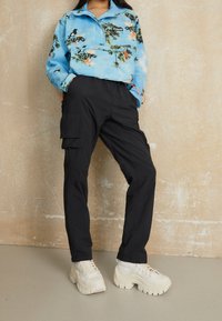 Light blue half-zip jacket with floral print, black cargo pants with pockets, and white chunky sneakers. Smooth fabric and relaxed fit.