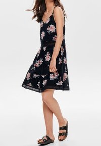 Schwarzes Blumenkleid mit verstellbaren Spaghetti-Trägern, schichtweise gestaltet und mit Spitzenbesatz, kombiniert mit schwarzen Sch Slide-Sandalen.