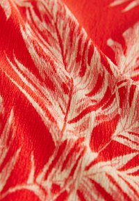 Textile featuring a vibrant red background with a white leaf pattern, textured surface, and prominent, flowing designs in contrasting colors.