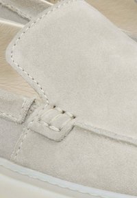 Světle šedá semišová nazouvací bota se šitým svrškem, texturovaným povrchem, zaoblenou špičkou a bílou gumovou podrážkou.