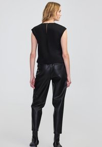 Schwarzes ärmelloses Top mit einem Schlüsselloch-Detail auf dem Rücken, kombiniert mit schwarzen Kunstlederhosen. Glatte Textur mit einer strukturierten Passform.