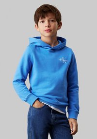 Sudadera con capucha azul hecha de suave tela de algodón, con un logo en la parte frontal y puños acanalados. Combinada con jeans de mezclilla oscura.