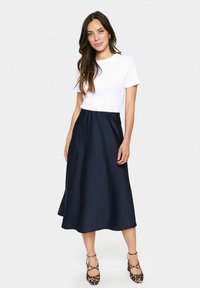 Jupe en satin navy avec une taille élastique, associée à un t-shirt blanc ajusté. Les chaussures présentent un imprimé animal et des brides à la cheville.