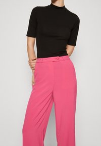 Czarny golf z krótkim rękawem w połączeniu z różowymi, szerokimi spodniami z wysokim stanem, wykonanymi z gładkiego materiału i zapinanymi z przodu na guziki.