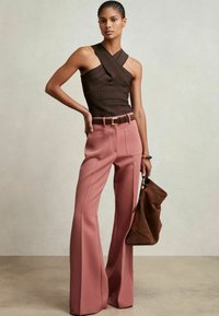 Hnedý textúrovaný halter top s prekrývajúcimi sa ramienkami, skombinovaný s vysokými ružovými zvonovými nohavicami a hnedou semišovou kabelkou.