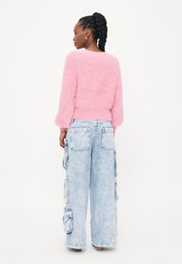 Fluffy roze trui met ballonmouwen, gecombineerd met lichtblauwe, losse cargobroeken met grote zakken en een vervaagde afwerking.