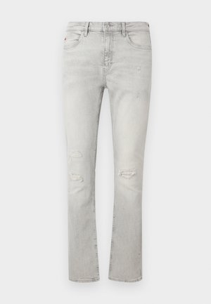 Jean slim gris clair avec usure aux deux genoux, cinq poches, fermeture par bouton et zip.