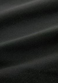 Zwarte stof met een gladde textuur, met subtiele ribbels en zachte plooien. Het materiaal lijkt duurzaam en licht elastisch.