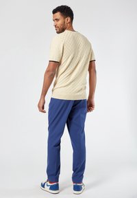 Suéter de punto beige con un patrón texturizado, detalles en azul marino en los puños, combinado con pantalones azules y zapatillas azules.