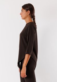 Maglietta marrone a maniche lunghe con scollatura rotonda e orlo asimmetrico, realizzata in un tessuto morbido e con una vestibilità comoda. Design semplice senza motivi visibili.