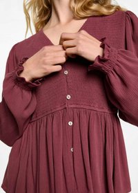 Pflaumenfarbige Bluse mit strukturierter Blende, Rüsche an den Ärmeln und Knopfleiste. Fließendes Design mit Falten an der Taille.