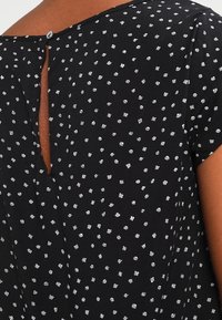 Czarna tkanina w białe kropki, krótkie rękawy i otwór w kształcie łezki z tyłu, zapinany na guzik.