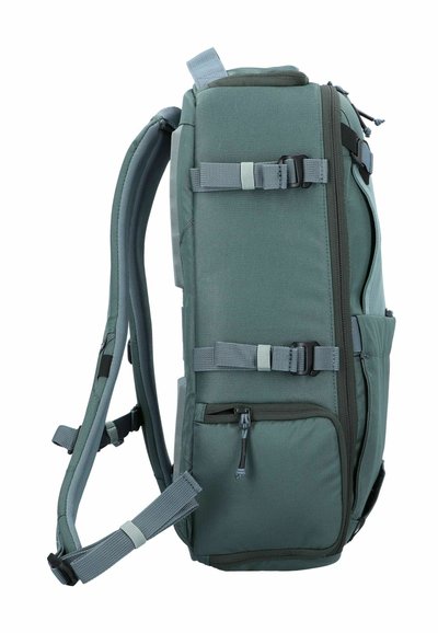 Zaino in tessuto verde con spallacci regolabili, molteplici fibbie, tasche laterali e superficie testurizzata. Presenta un comparto con zip sulla parte anteriore.