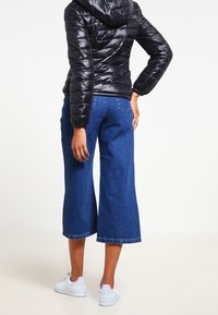 Sort pufferjakke med hætte, kombineret med blå cropped denimbukser. Modellen har hvide sneakers på. Glat tekstur og afslappet design.