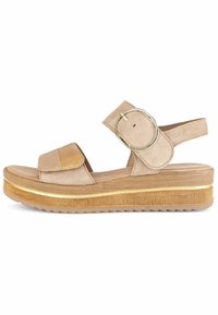 Sandalo in suede beige con una larga cintura, fibbia circolare e suola piatta testurizzata con un accento dorato. Suola piatta con dettagli antiscivolo.