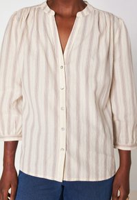 Donna che indossa una blusa a righe color crema, con maniche a sbuffo tre quarti, e jeans blu.