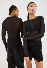 Schwarzes langärmeliges, durchscheinendes Oberteil mit kurvenförmigem Taillenschnitt, kombiniert mit schwarzen Shorts und eleganten Accessoires. Glatte Textur, figurbetontes Design.