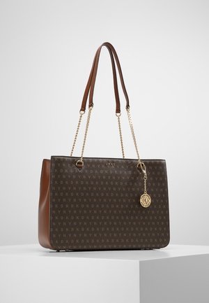 Brązowa torba typu tote marki DKNY z monogramem, złotym łańcuszkiem i skórzanymi paskami na ramię oraz okrągłą złotą zawieszką z logo z przodu.