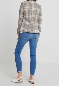 Blazer à carreaux aux couleurs claires, coupe ajustée, avec des boutons en accent, associé à un jean skinny bleu et des talons blancs à brides.