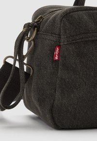 Donkergrijze stoffen tas met een vierkante vorm, textuur oppervlak, bovenste ritssluiting en een rode Levi's-label. Inclusief een schouderband en metalen hardware.