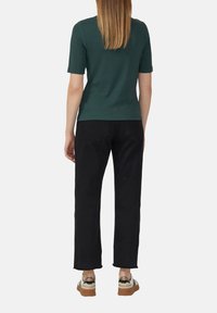 Donkergroene slim-fit t-shirt met korte mouwen gecombineerd met zwarte recht-toe-rechtdoor spijkerbroek, met een rafelige zoom en beige sneakers met zwarte accenten.