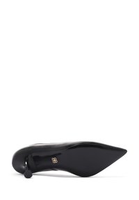 Zapato de tacón alto negro con punta afilada, textura de cuero suave y un acento dorado cerca del tacón. La suela es plana y ligeramente redondeada.