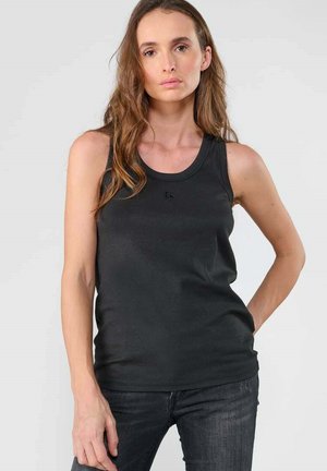 Camiseta sin mangas de canalé negra con escote redondo y tirantes finos, con un pequeño logo en la parte delantera. Combinada con jeans oscuros.