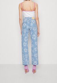 Vrouw in lichtblauwe denim jeans met grote witte bloemenprints, een witte tanktop met roze bandjes en roze hoge hakken.