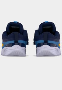 Ζευγάρι μπλε και κίτρινα παιδικά αθλητικά παπούτσια από πίσω, με λευκές σόλες και επενδεδυμένα περιλαίμια αστραγάλου σε απλό φόντο.