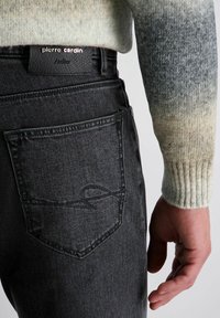 Zwarte denim jeans met een platte achterpocket met een subtiele logo-stiksel. De stof lijkt iets textuur te hebben, met een duidelijke aangesloten pasvorm.
