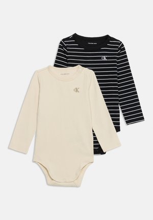 Deux bodies pour bébé à manches longues, un beige uni et un noir avec des rayures blanches, tous deux avec un petit logo "cK" sur la poitrine.