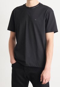 T-shirt nera in cotone con collo rotondo, maniche corte e un piccolo logo ricamato "ck" sul petto, con marchio Calvin Klein sul colletto.
