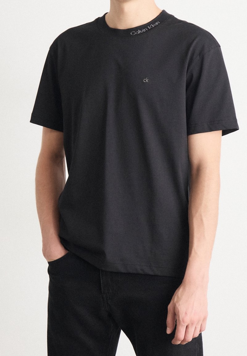 T-shirt nera in cotone con collo rotondo, maniche corte e un piccolo logo ricamato "ck" sul petto, con marchio Calvin Klein sul colletto.