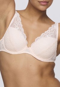 Koronkowy biustonosz w delikatnym różu, z kwiatowym wzorem, przejrzystym materiałem, szerokimi falbaniastymi ramiączkami oraz małą kokardką na środku.