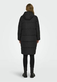 Abrigo inflado negro con capucha, que presenta un diseño cuadrado, costuras horizontales y un corte de longitud media, complementado con leggings negros y botas.