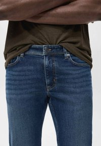 Jeans de mezclilla azul oscuro con corte recto, que presentan un diseño clásico de cinco bolsillos, cierre de botón metálico y sutiles detalles de desgarro.