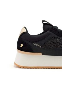 Sneaker nera con un pannello laterale in mesh testurizzato, puntale solido, suola piatta bianca e dettagli dorati sul retro.