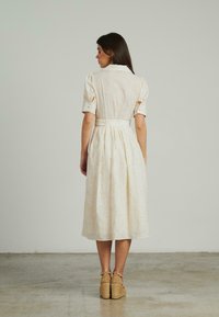 Abito bianco al ginocchio con maniche corte, tessuto texturizzato, vita aderente e gonna plissettata, abbinato a zeppe espadrilles color sabbia.