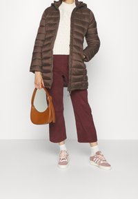Manteau matelassé marron avec coutures verticales, capuche, pull en maille écru, pantalon bordeaux à jambes larges, sac à main marron et baskets roses.