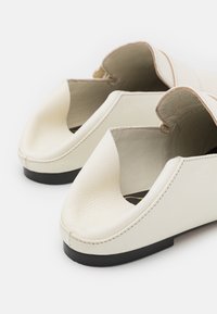 Vita läderöppna skor med en strukturerad yta, konturerad form och minimal svart sula. Har en delad design vid framfoten.