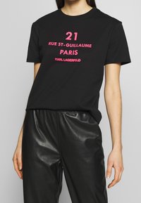 Czarna bawełniana koszulka z odważnym różowym napisem: "21 RUE ST-GUILLAUME PARIS KARL LAGERFELD." Krótkie rękawy, okrągły dekolt, luźny krój.