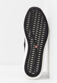 Sort gummisul med et mønstret slidbane-design, der har en hvid kant og en rød logo detalje nær midten.